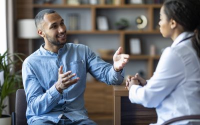 Handsome african american young man having appointment with female doctor, looking at black woman therapist, gesturing and smiling, modern clinic interior, copy space