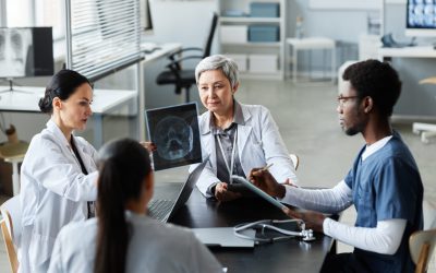 Group of intercultural radiologists discussing scalp x-ray results of patient with traumatic brain injury while sitting by table in medical office
