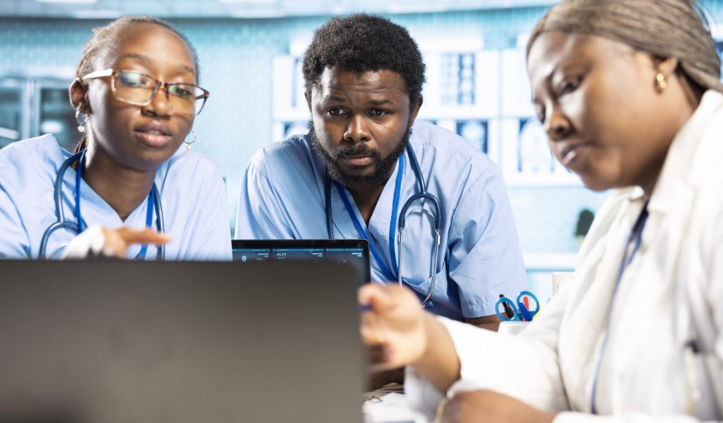 Group of healthcare specialists in scrubs analyzing results with doctor, emphasizing teamwork, professional training and care management in a modern office. Medical staff doing research.