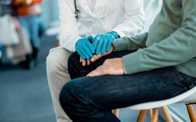 Unrecognizable doctor wearing protective glove while comforting senior patient in a hallway at medical clinic.